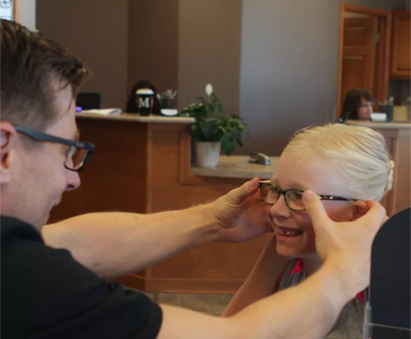 optometrist giving young girl glasses